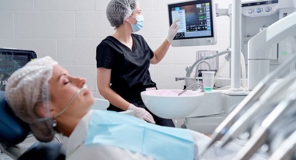 Patient undergoing sleep dentistry procedure with a dentist monitoring vitals on a screen in a modern dental clinic